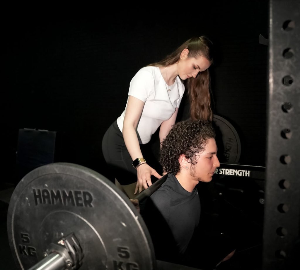 Personal Trainer trainiert jungen Mann mit Langhantel